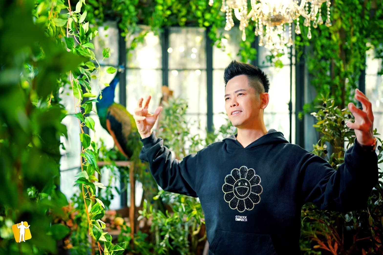 佳興老師穿黑色上衣,在綠色植栽與吊燈背景前張開雙手